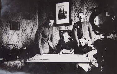Sztab IV odcinka frontu w Kcyni. Fotografia 4. os&oacute;b w pomieszczeniu przy stole z rozłożoną mapą. Rok 1919. Ze zbior&oacute;w Archiwum Państwowego w Poznaniu (z zespołu KW PZPR w Poznaniu, sygn. 16897)